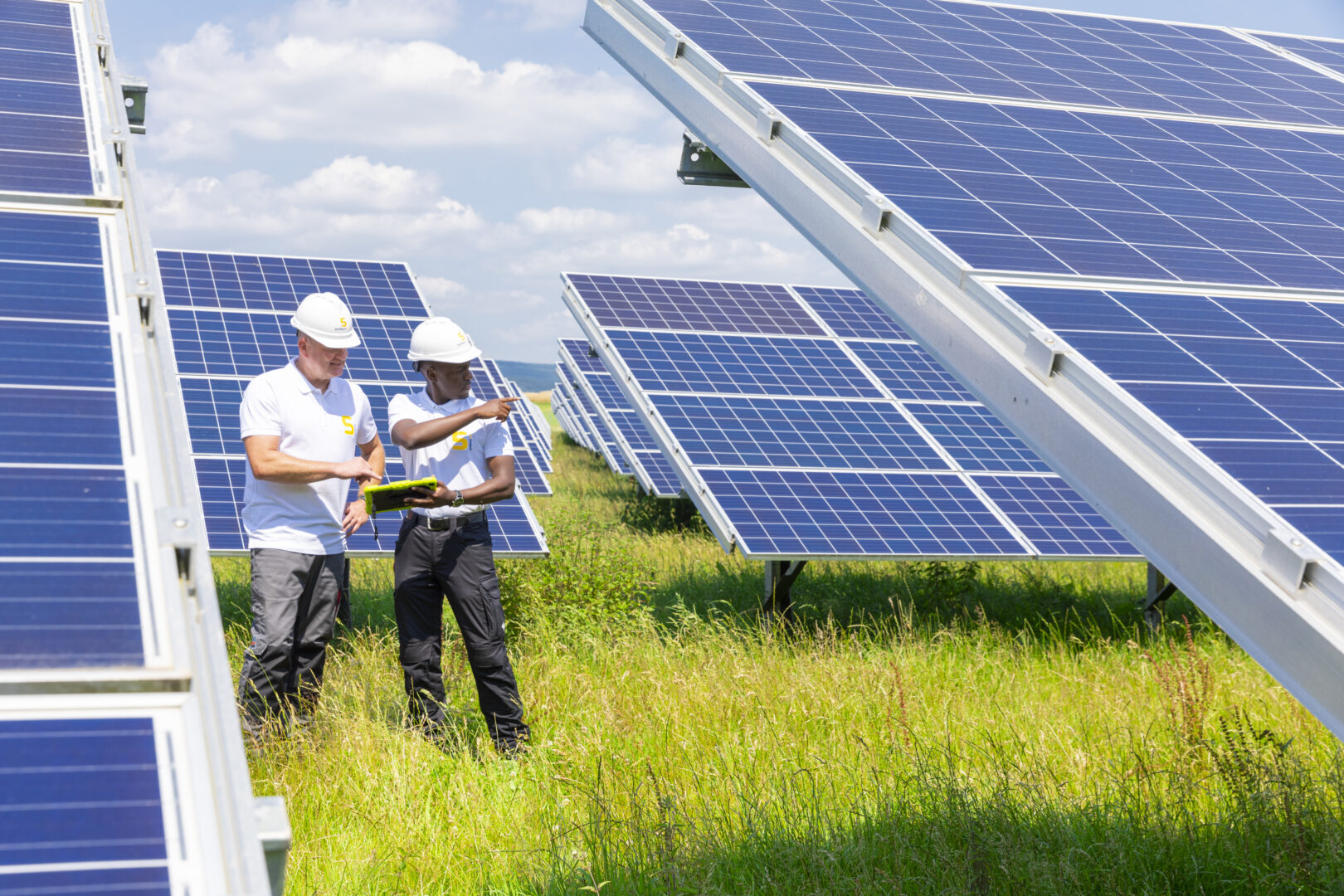 Zwei Techniker von GOLDBECK SOLAR stehen auf einer Wiese zwischen den Solarpanels einer Photovoltaikanlage.